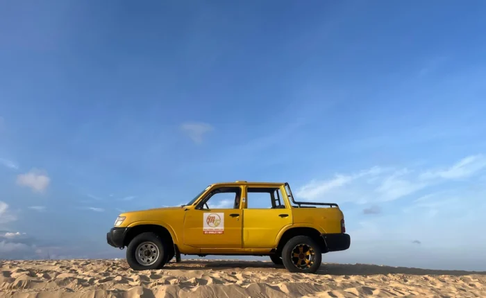 Tourists exploring Bau Trang White Sand Dunes on a jeep, with golden sand dunes and a blue lake in the background.
