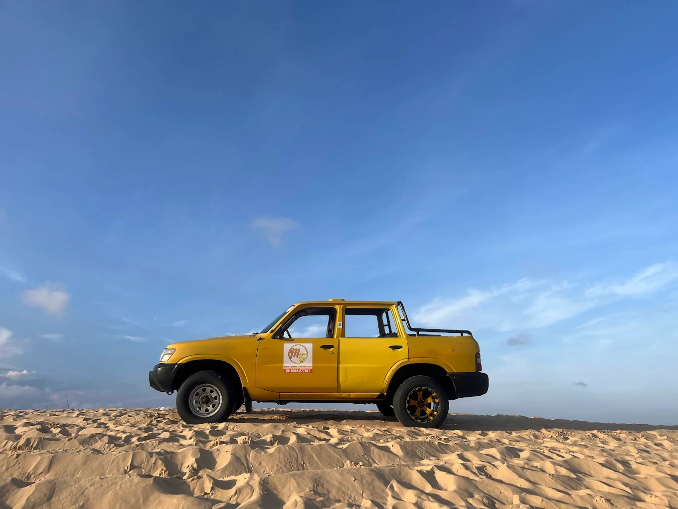 Tourists exploring Bau Trang White Sand Dunes on a jeep, with golden sand dunes and a blue lake in the background.