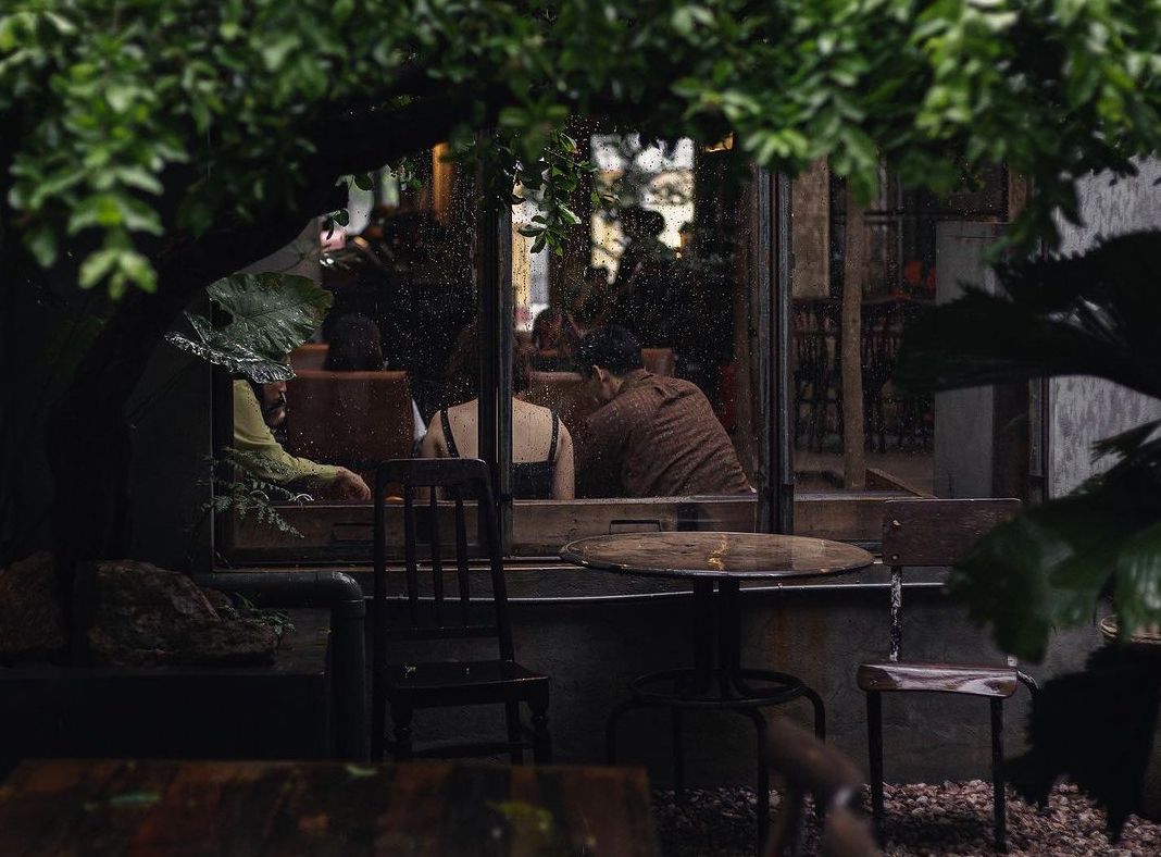 A cozy cafe in Hue with customers sipping coffee while watching the rain outside.